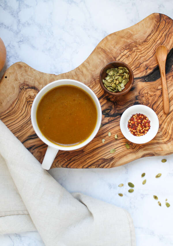 soup in a bowl with pumpkin seed garnish and red pepper flakes in dipping bowls