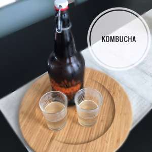 A tray with a bottle of kombucha and 2 glasses half full