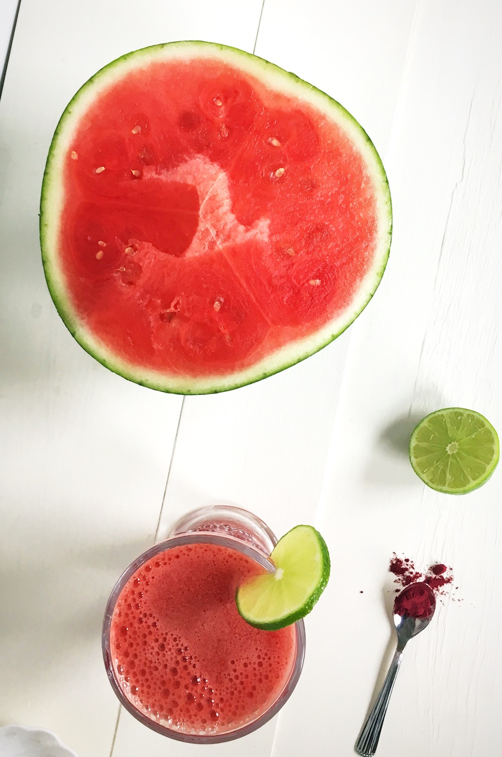 half cut watermelon, a half a lime and beetroot powder. A glass of watermelon juice is also nearby.
