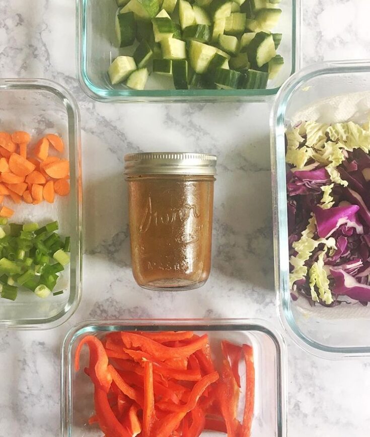 meal prep containers filled with vegetables and peanut dressing in the center