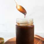 A hand reaching into a jar of imli/tamrind chutney