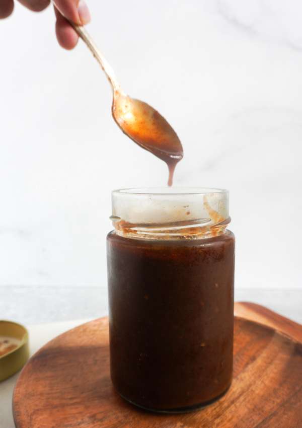 A hand reaching into a jar of imli/tamrind chutney