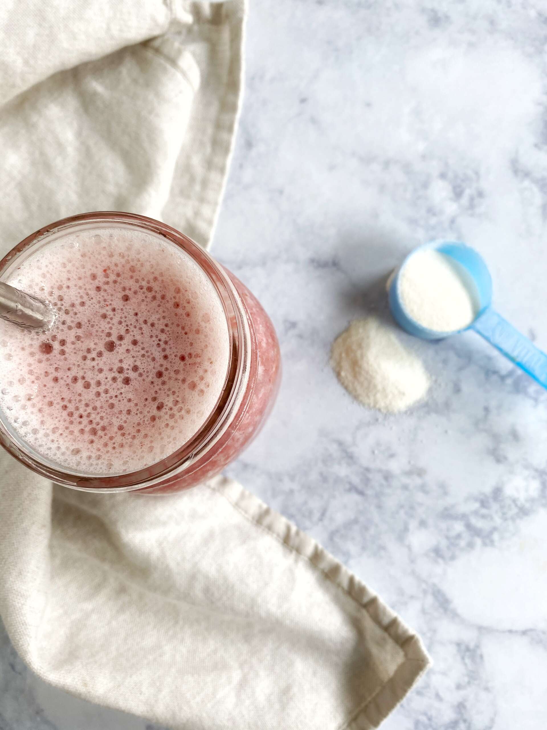 glass of smoothie with a scoop of collagen peptide next to it