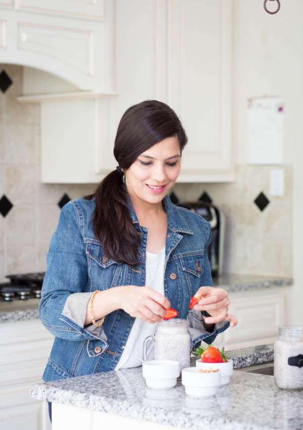 a woman topping chia pudding container with strawberries