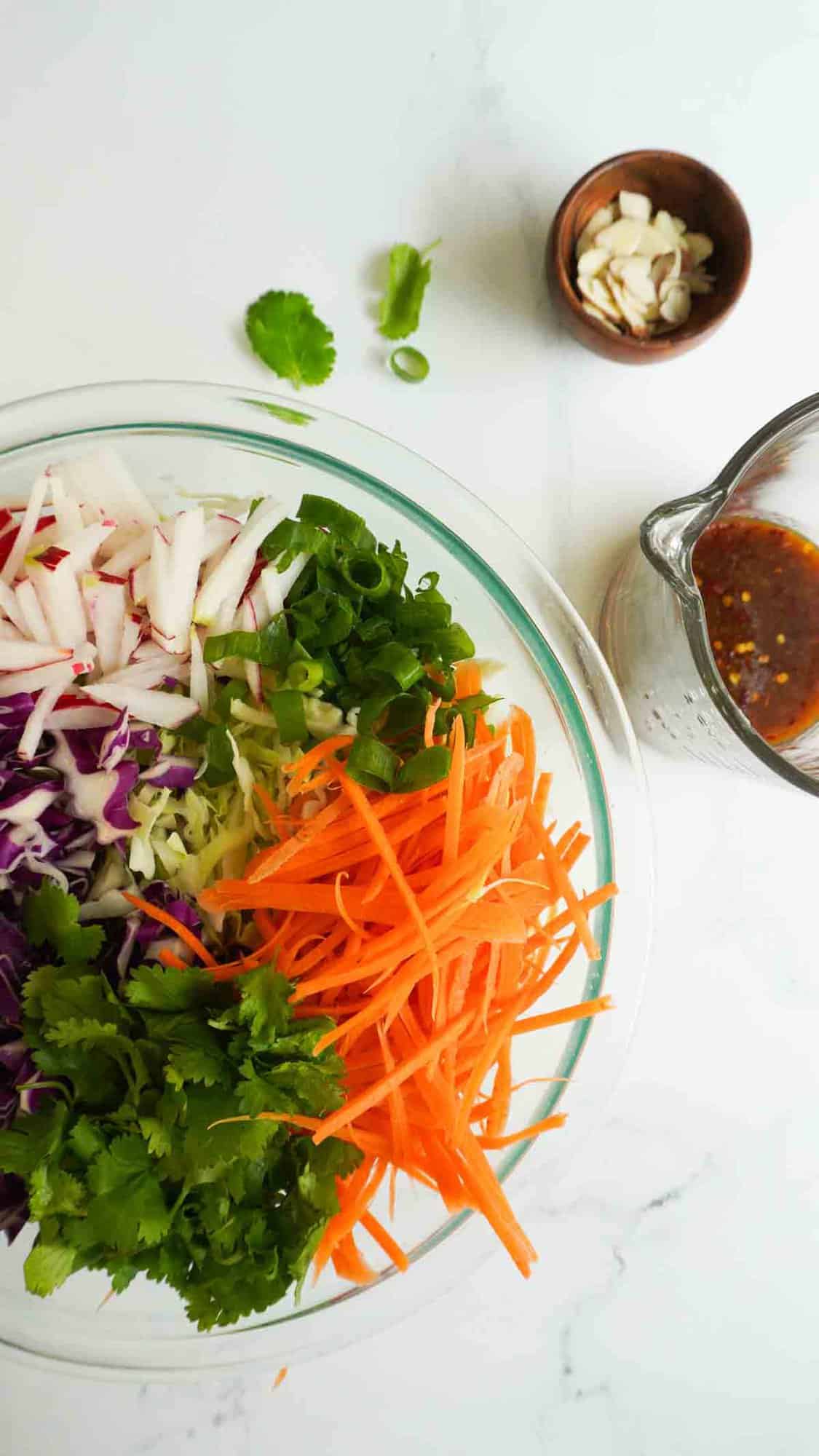 A bowl with thai salad ingredients with dressing to the side and some almonds in a dipping bowl