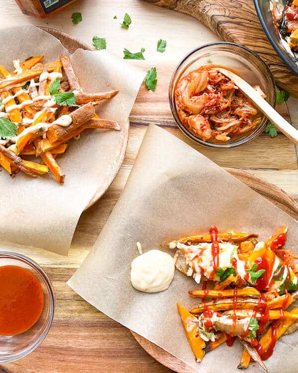 two servings sweet potato fries with kimchi and hot sauce in condiment dishes