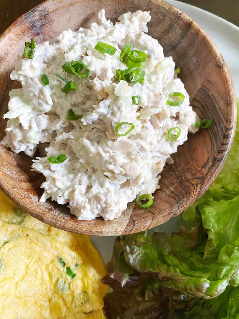 Chicken sandwich spread in a wooden bowl with a green onion garnish