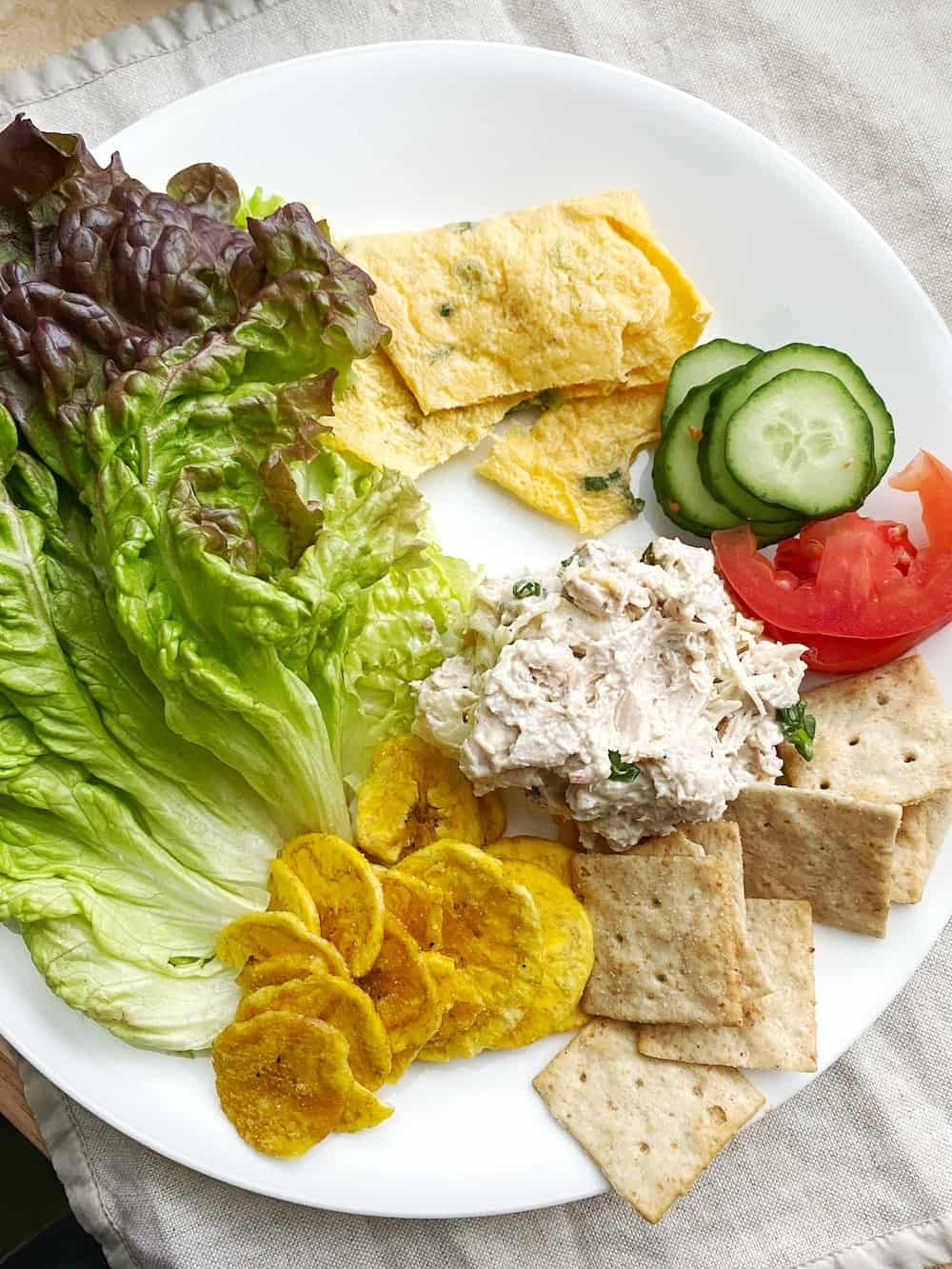 A plate with vegetables, chips, crackers and chicken sandwich spread