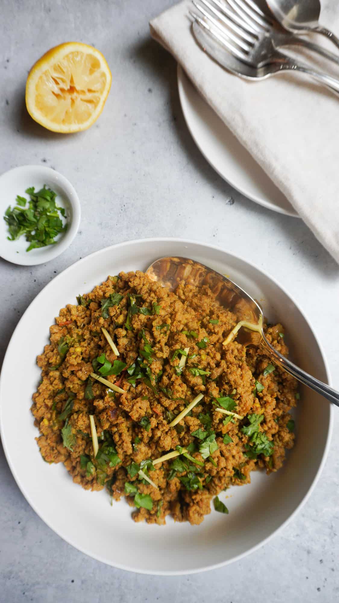 serving bowl of keema and plates, cutlery and napkins