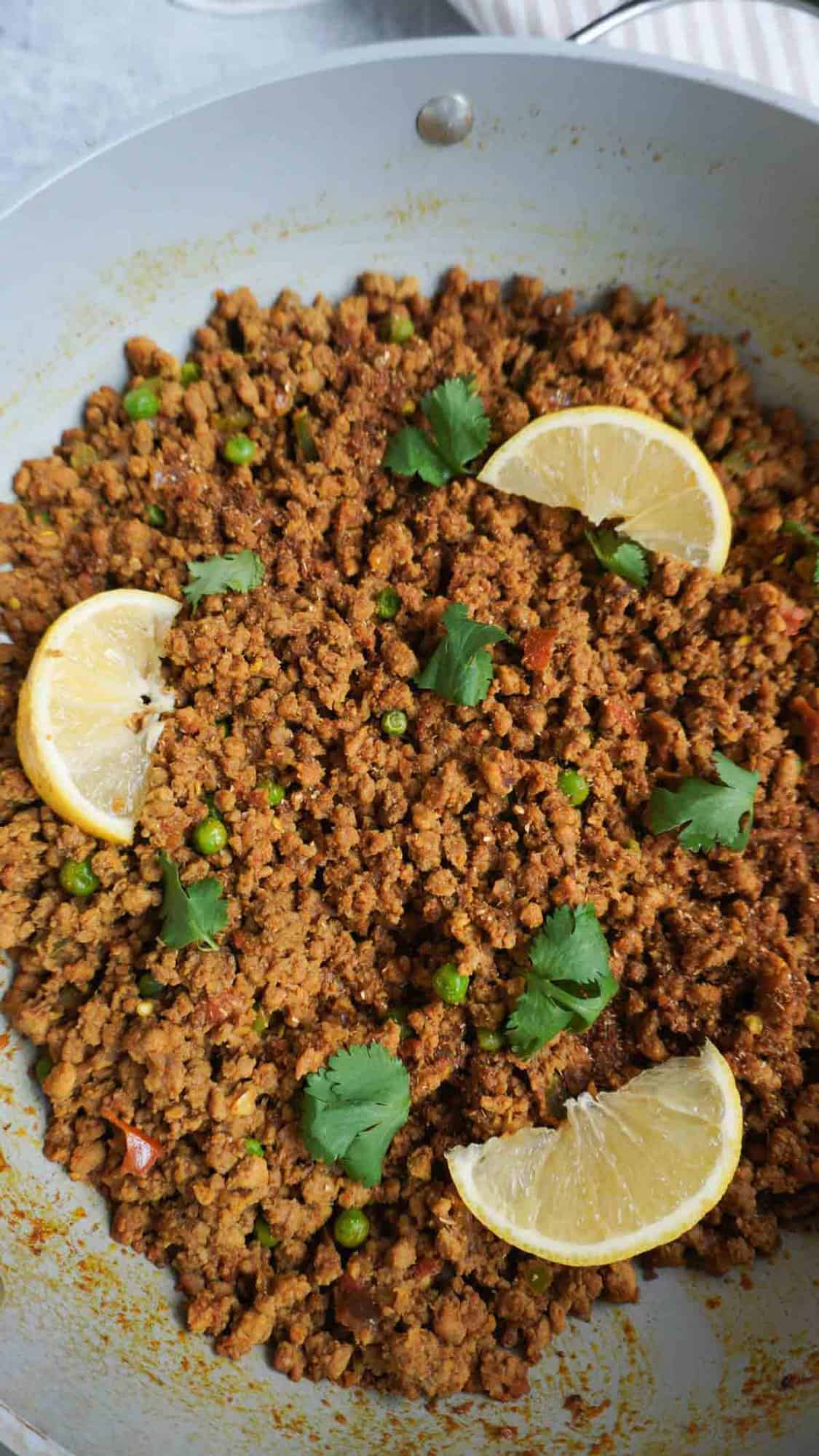 A pan with keema matar garnished with lemon slices and cilantro