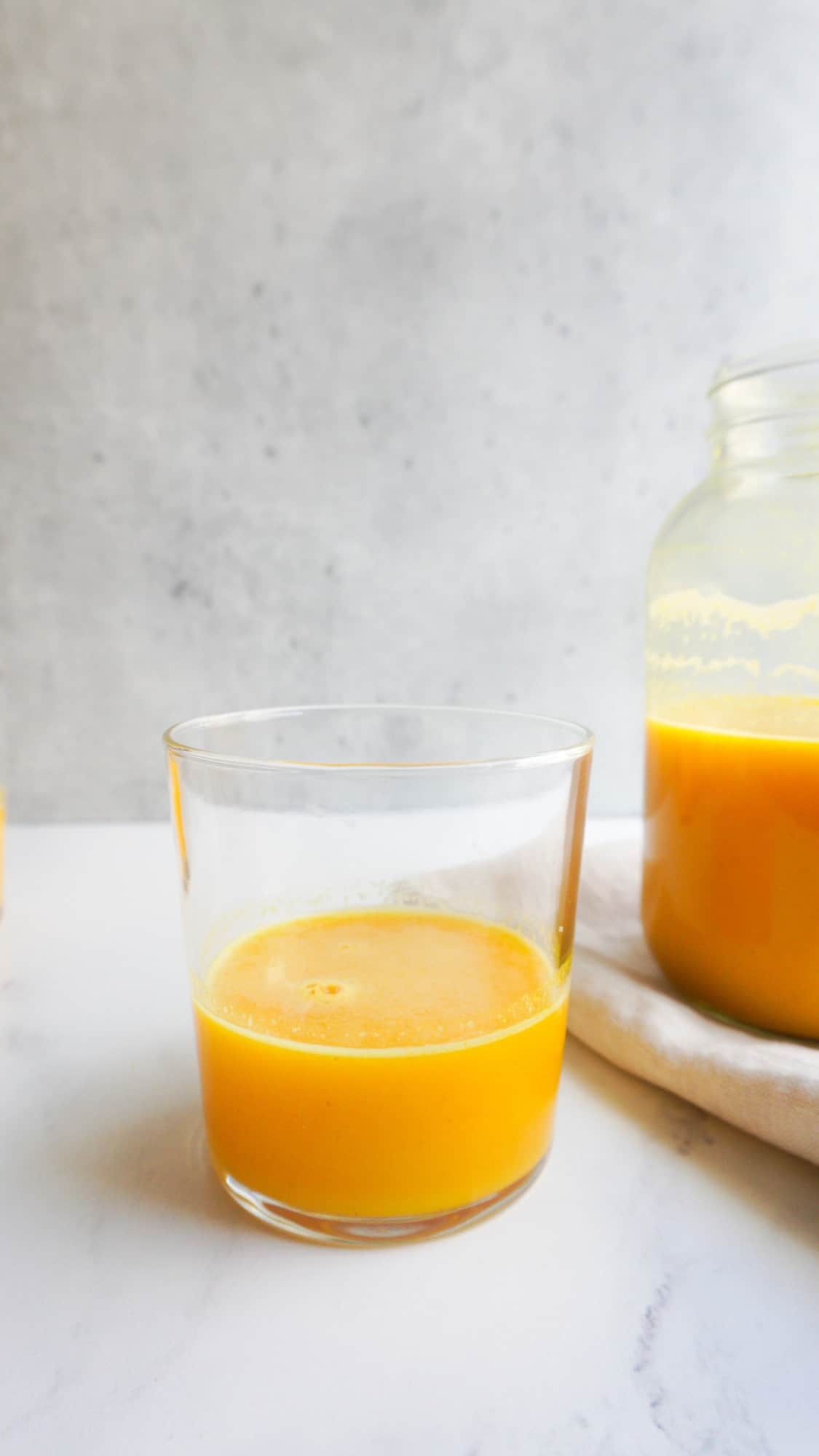 A glass and a mason jar filled with ginger turmeric immunity shot