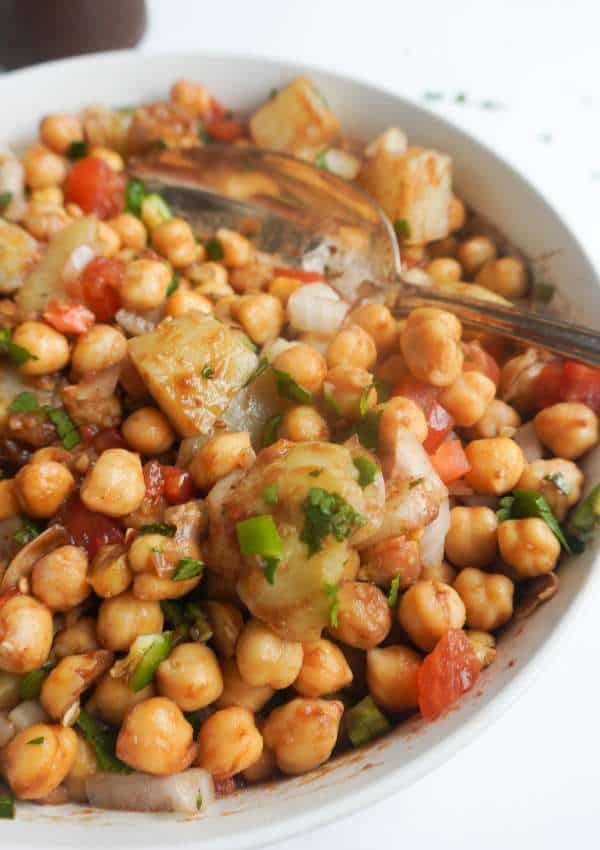 a serving bowl with chana chaat with diced tomatoes, onions, green chili and cilantro garnish