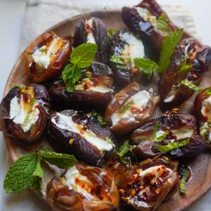 A plate of goat cheese stuffed dates drizzled with hot honey and mint leaves garnish