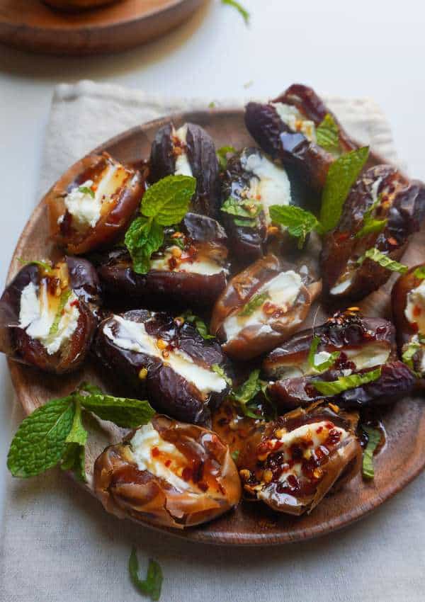 A plate of goat cheese stuffed dates drizzled with hot honey and mint leaves garnish