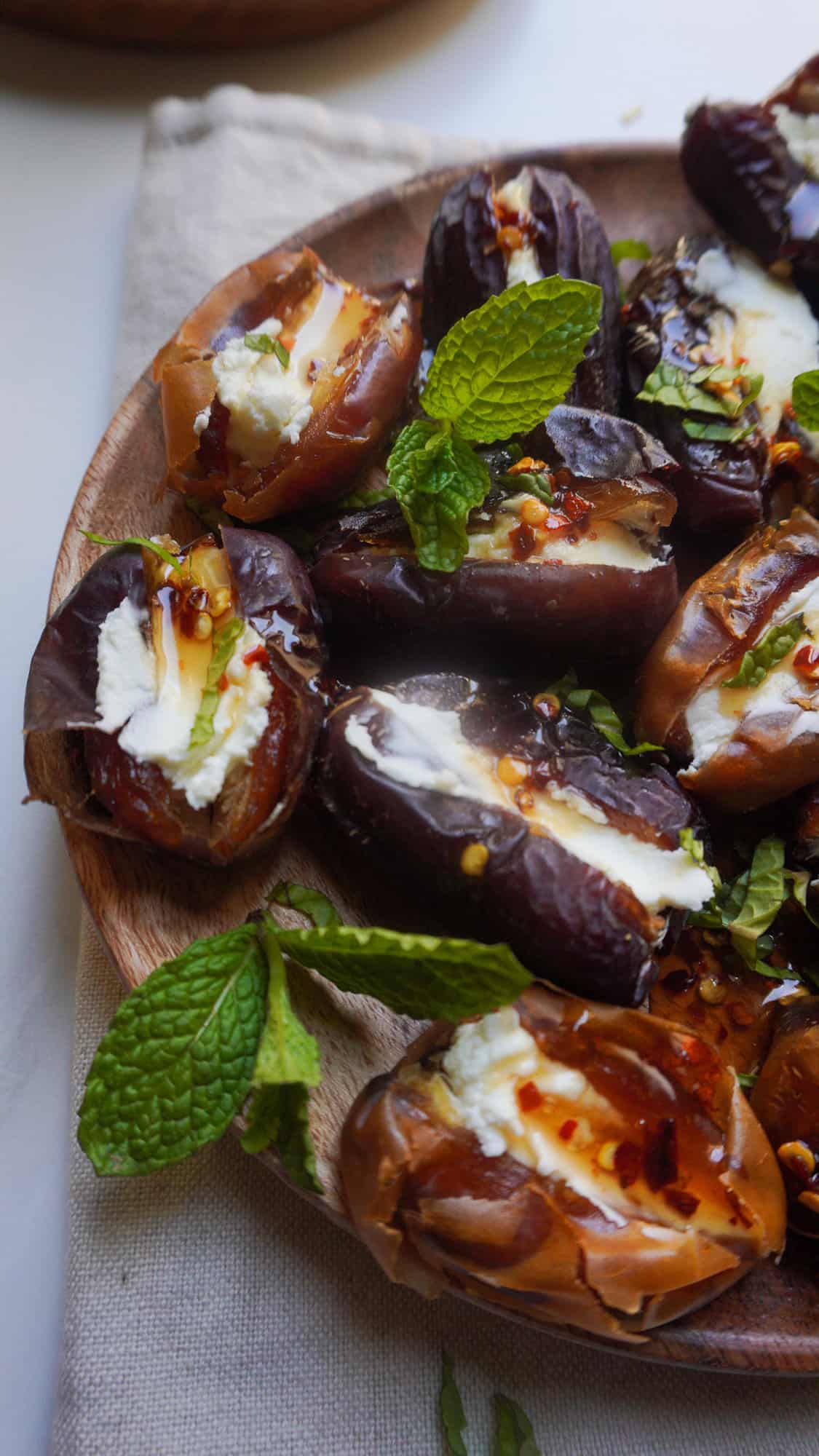 A plate of goat cheese stuffed dates with a drizzle of hot honey and sprigs of mint