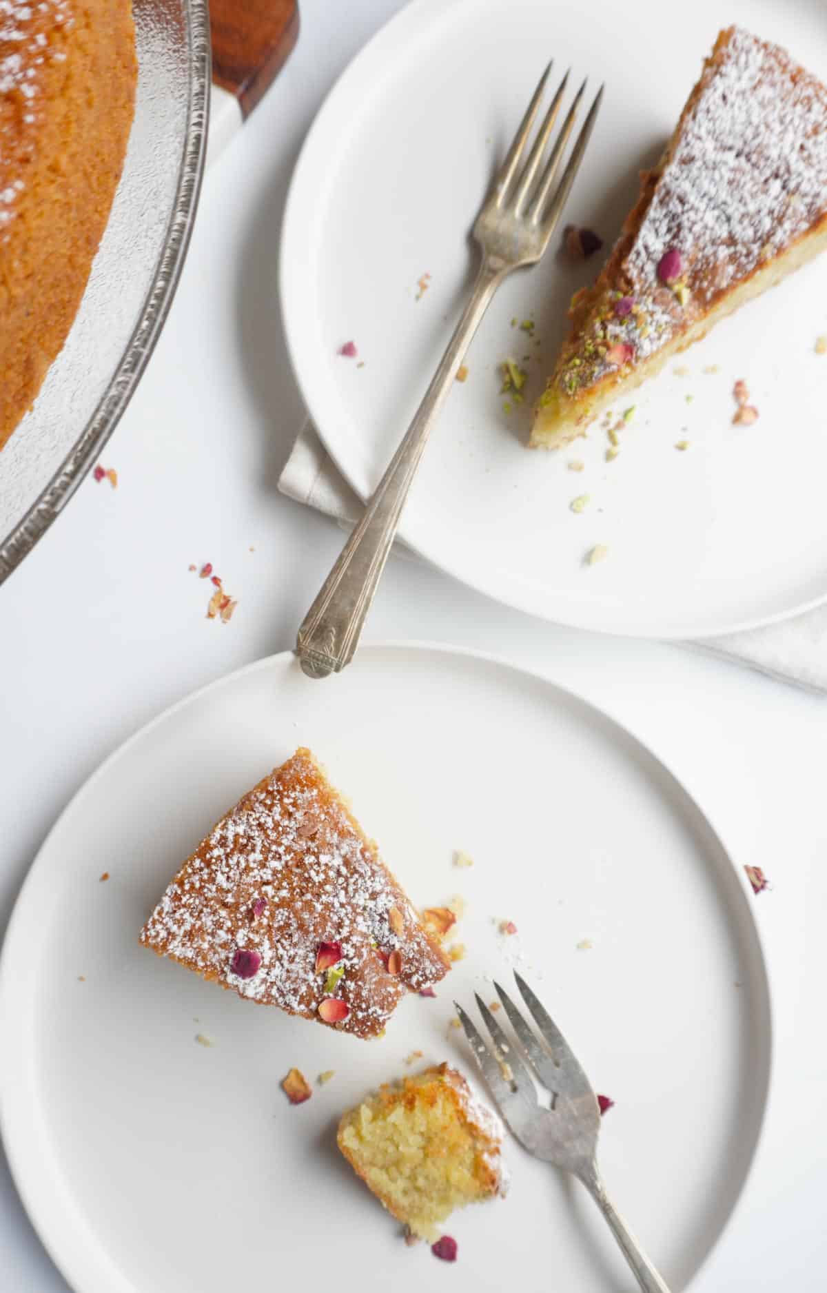 2 plates of gluten free cardamom cake with forks, a napkin and a cake platter on the side