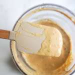 A spatula with spicy cashew butter dressing and a food processor with the dressing in the background