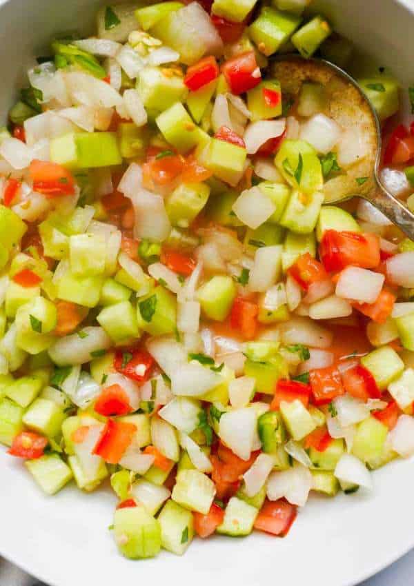 A bowl of finely diced tomatoes, onions, green chili and cucumbers. Seasoned with cilantro, lemon juice and salt