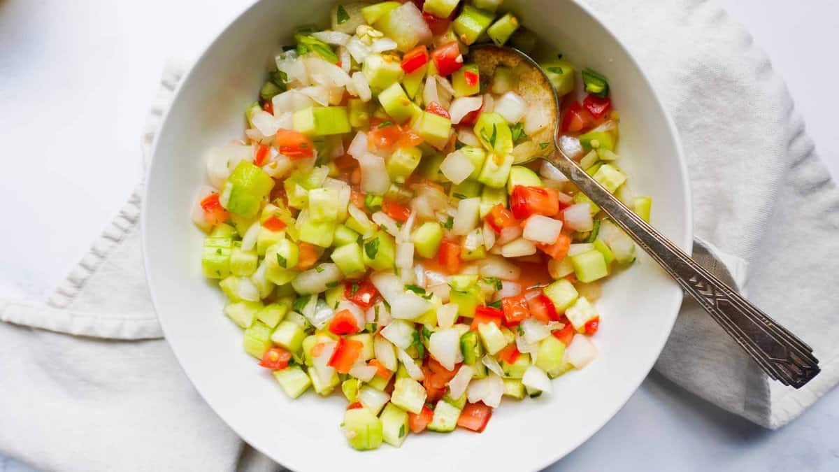 A bowl of finely diced tomatoes, onions, green chili and cucumbers. Seasoned with cilantro, lemon juice and salt