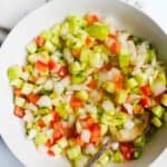 A bowl with diced vegetables on a light surface.