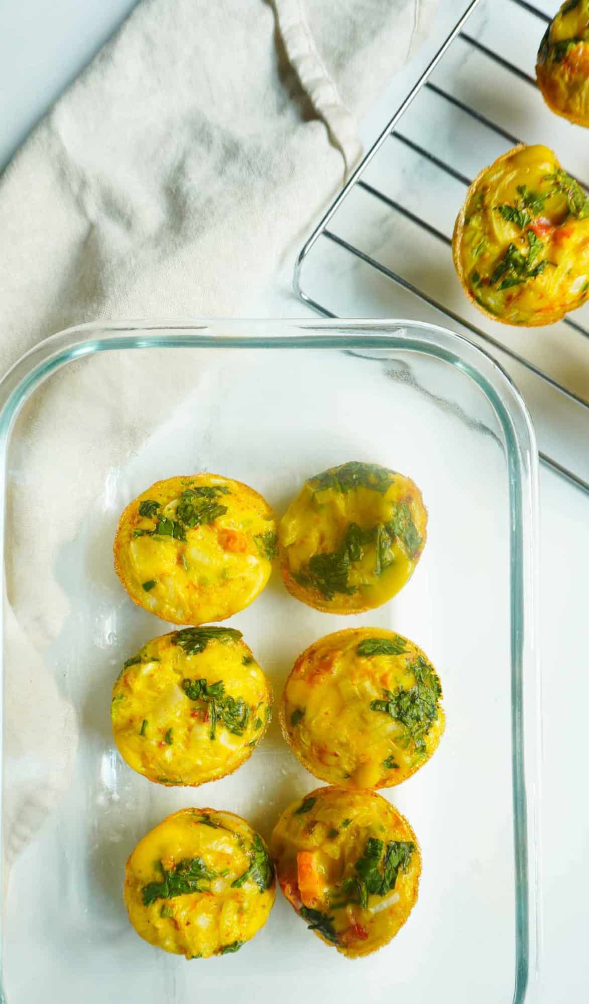 egg (khagina) muffins in a clear storage container with some on a wire rack to the side