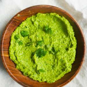 A small wooden bowl with Sweet Pea Chutney and a garnish of cilantro