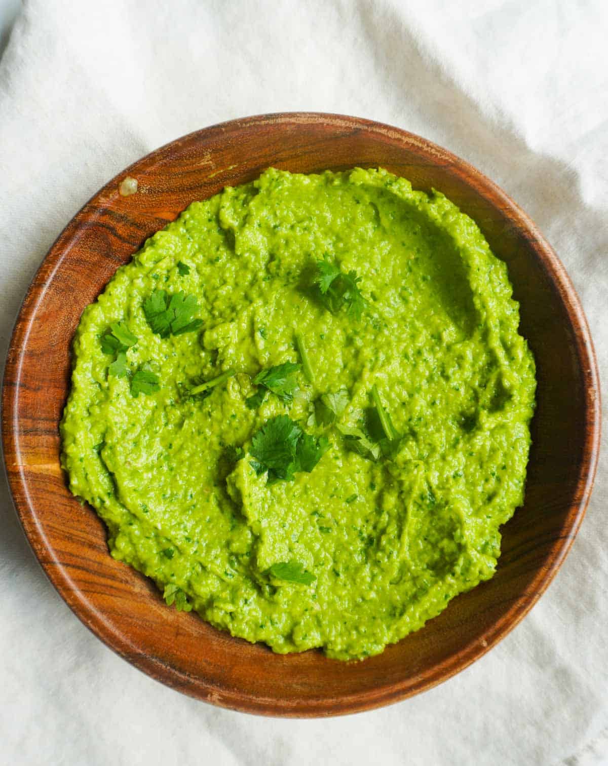 A small wooden bowl with Sweet Pea Chutney and a garnish of cilantro