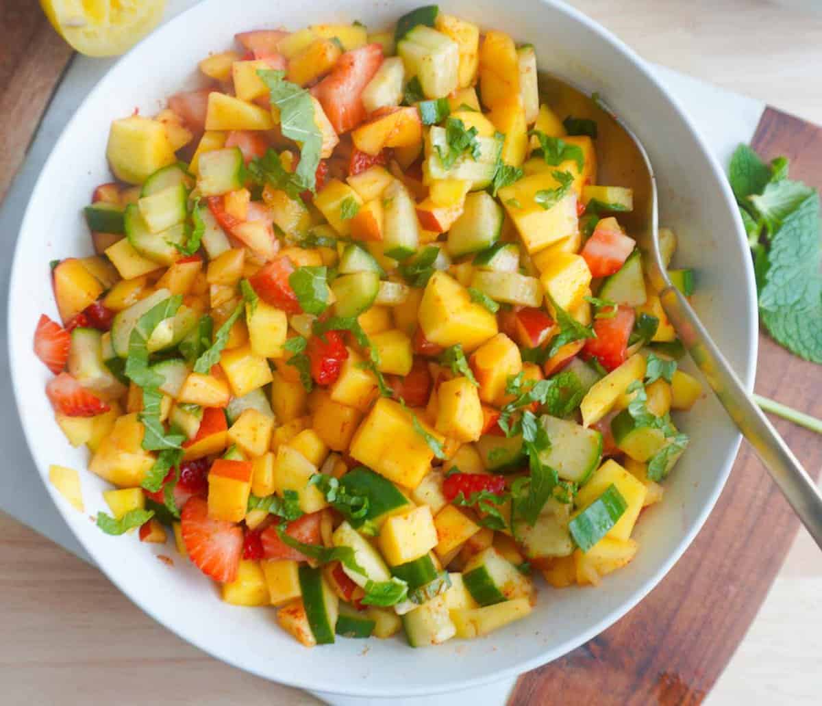 chopped mango, nectarine, cucumber and strawberries in a bowl with mint garnish. Squeezed lemon to the side and mint sprig