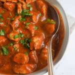 Tandoori chicken curry in a bowl with a serving spoon on top of off white napkin