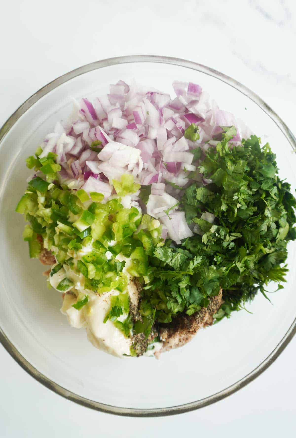 a bowl filled with canned tuna, cilantro, chopped red onion, jalapeno, salt and pepper