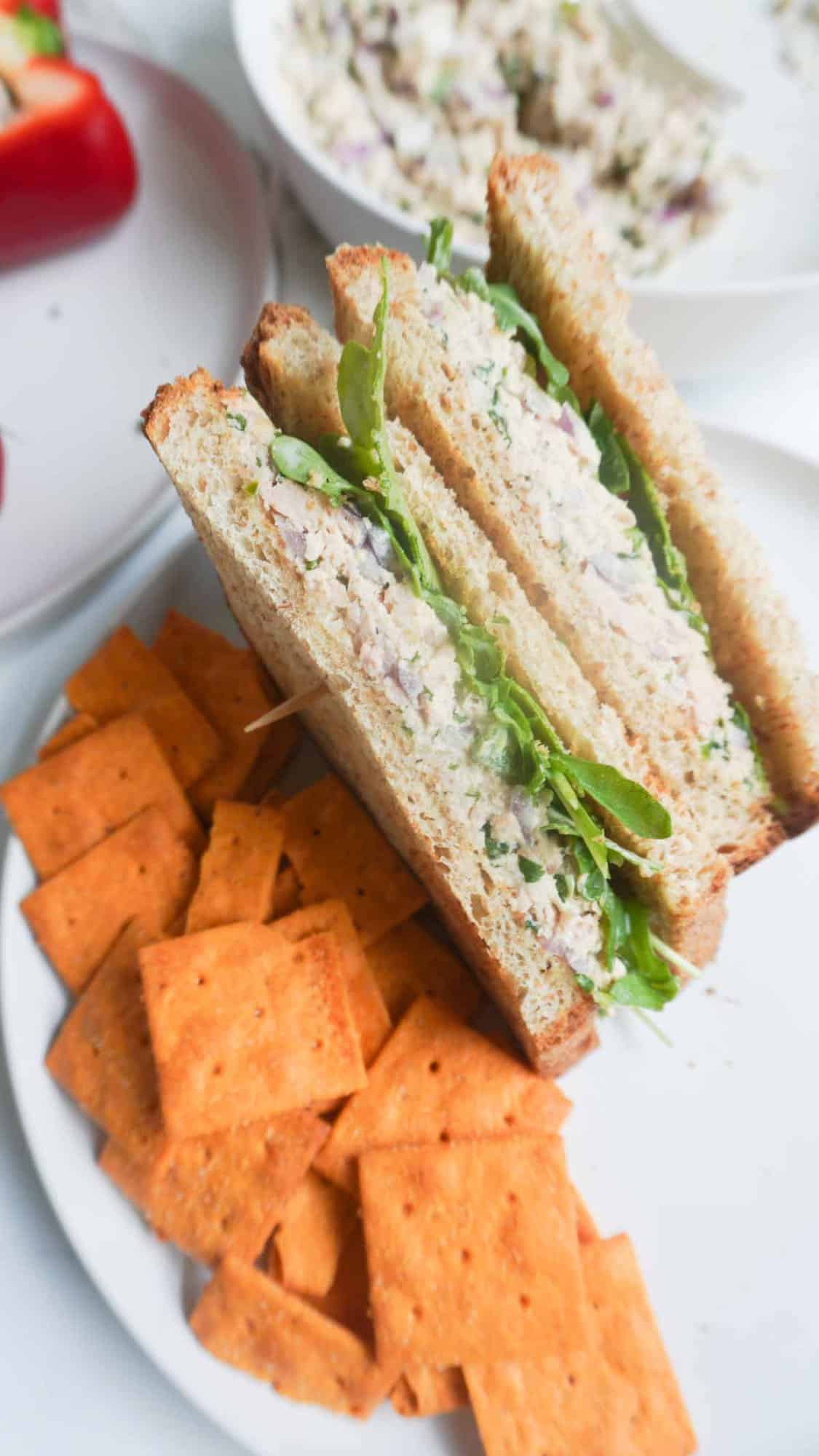 tuna salad sandwich on a plate with almond crackers and a bowl with tuna salad in the back ground as well as a plate with a partial view of red bell pepper