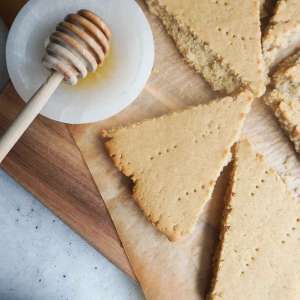 pieces oof baked flat bread on a wooden board and parchment with a small dipping bowl with honey and spoon to the side