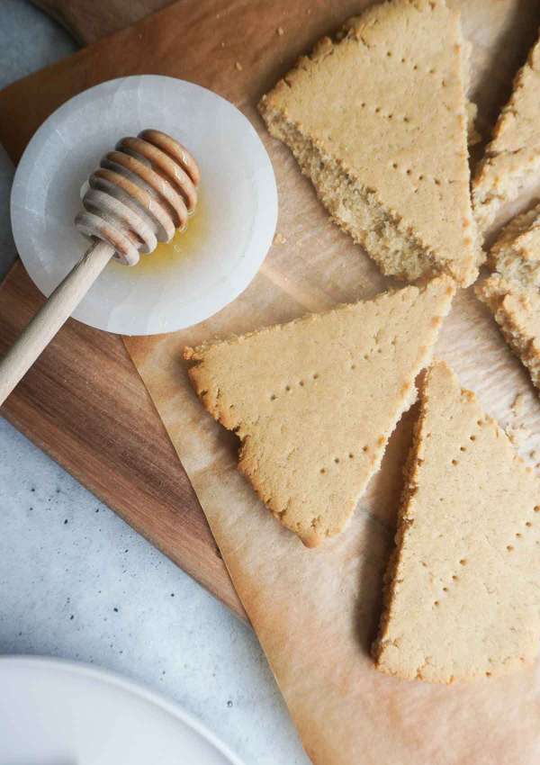 pieces oof baked flat bread on a wooden board and parchment with a small dipping bowl with honey and spoon to the side