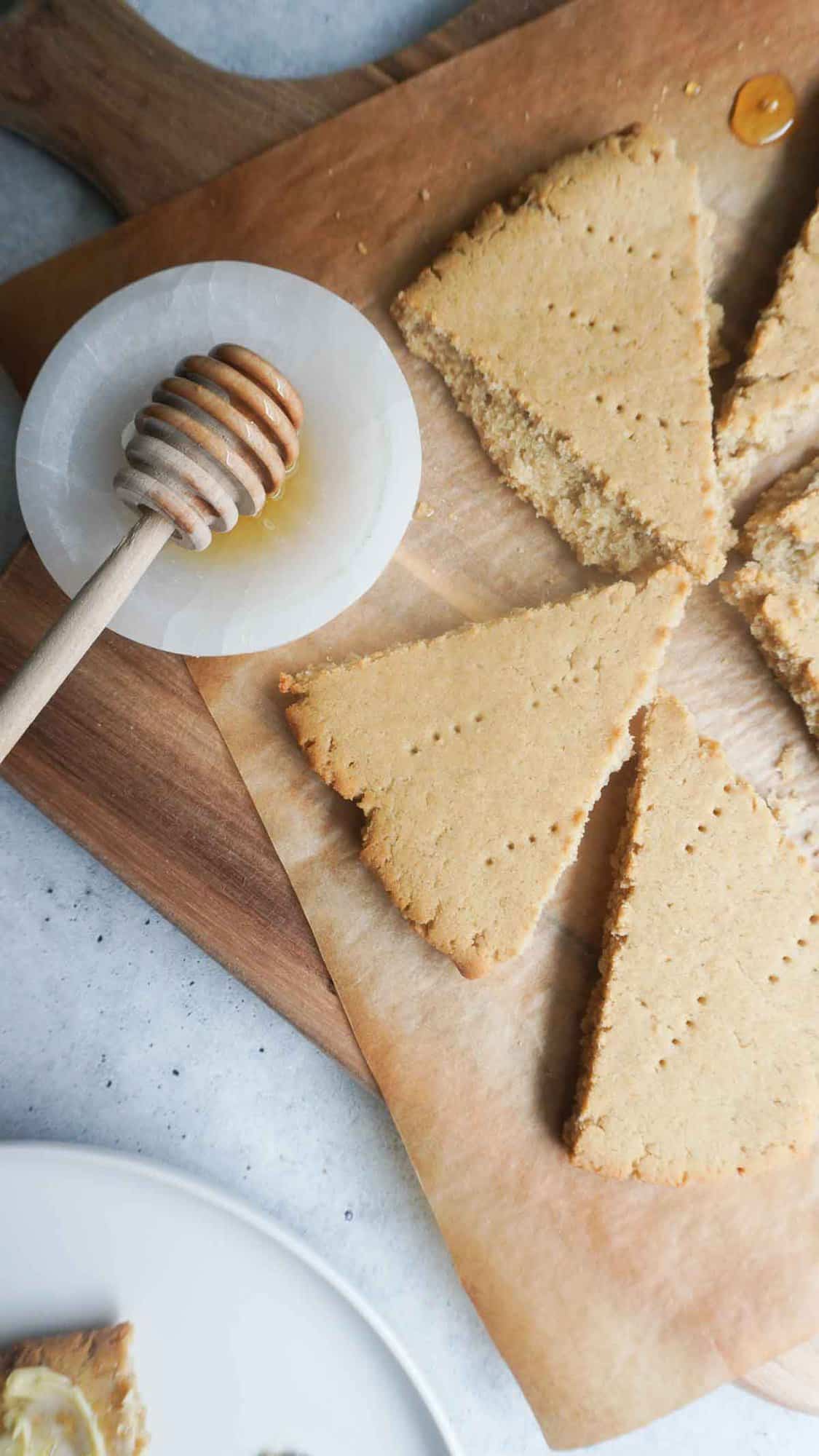 pieces oof baked flat bread on a wooden board and parchment with a small dipping bowl with honey and spoon to the side 