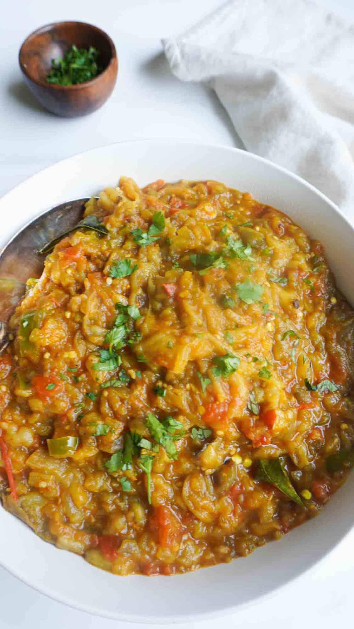 Oven roasted Baingan bharta in serving bowl and cilantro garnish in a small wooden bowl and napkin on the side