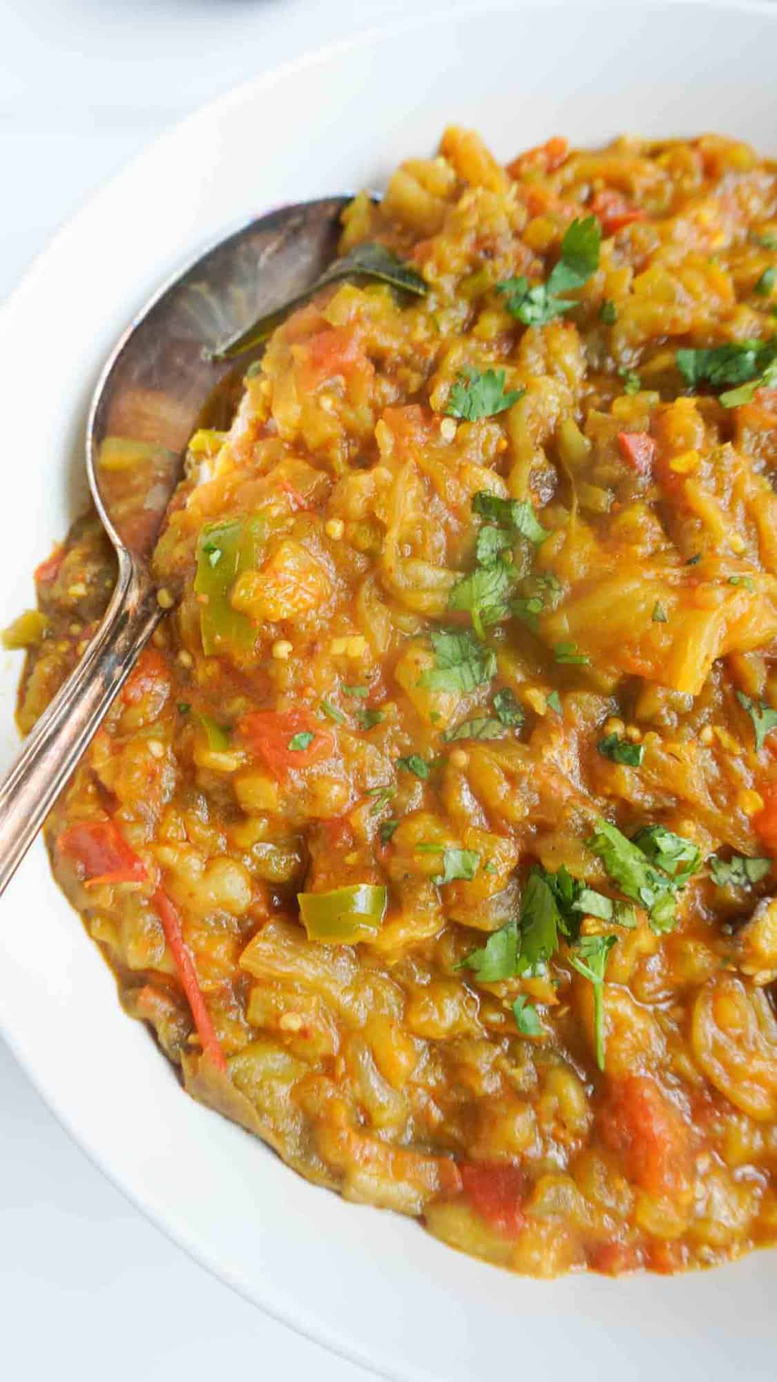 roasted aubergine curry in serving bowl with a spoon on the left side.