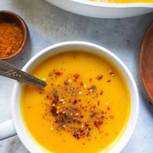 A single bow of soup and a pot in far right corner. A wooden spice bowl with turmeric