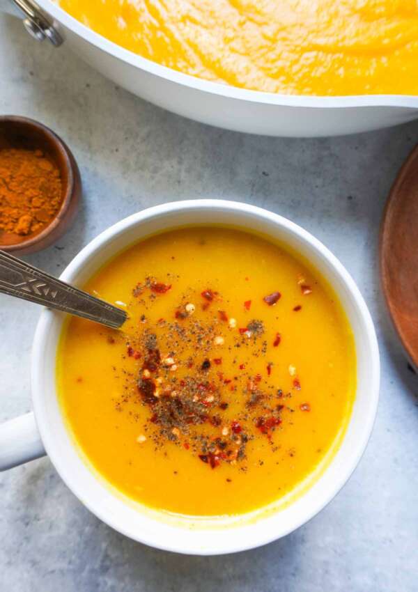 A single bow of soup and a pot in far right corner. A wooden spice bowl with turmeric