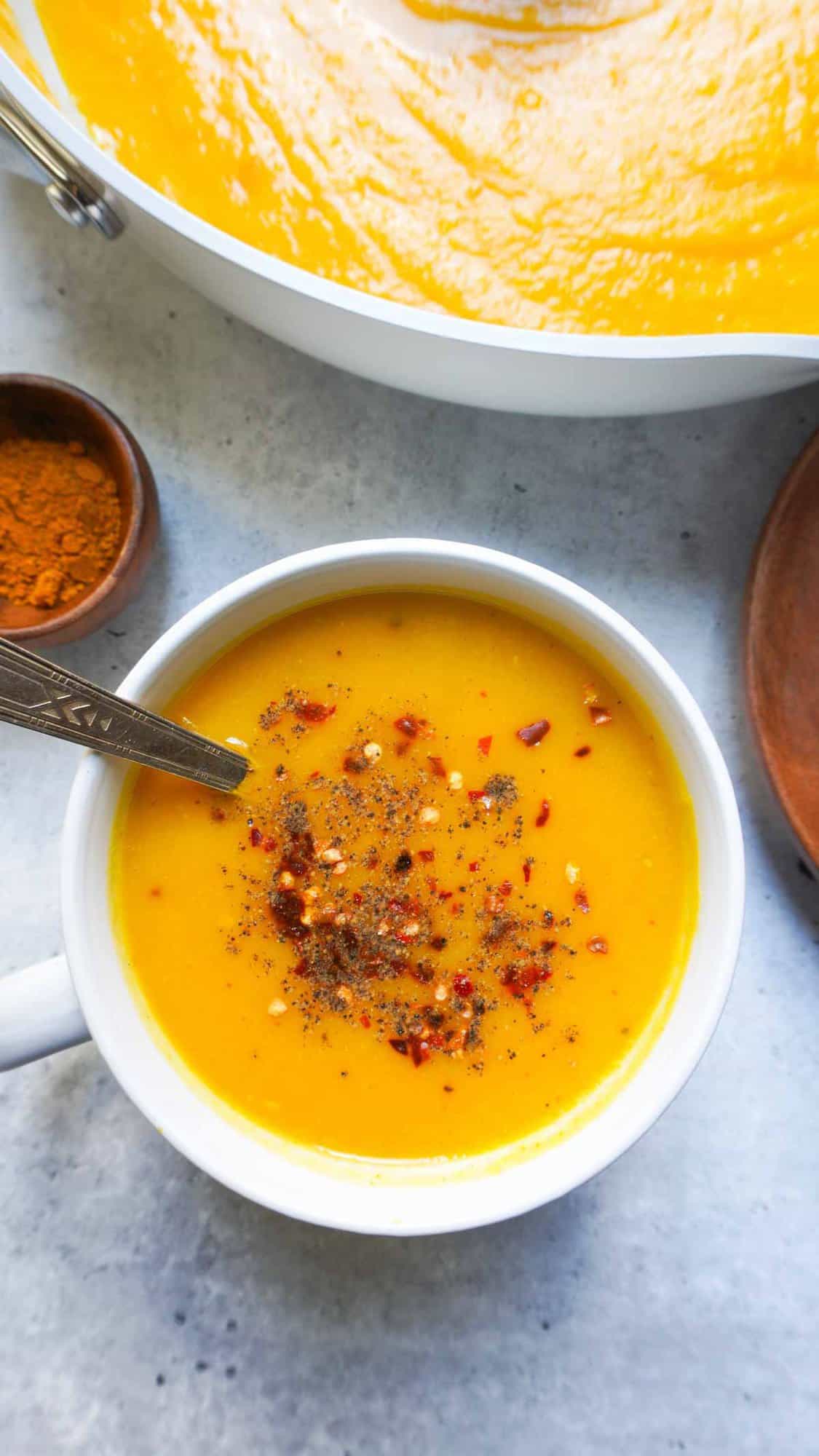 A single bow of soup and a pot in far right corner. A wooden spice bowl with turmeric