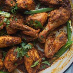 Karahi Chicken in a cast iron pan garnished with juliened green chilies and cilantro