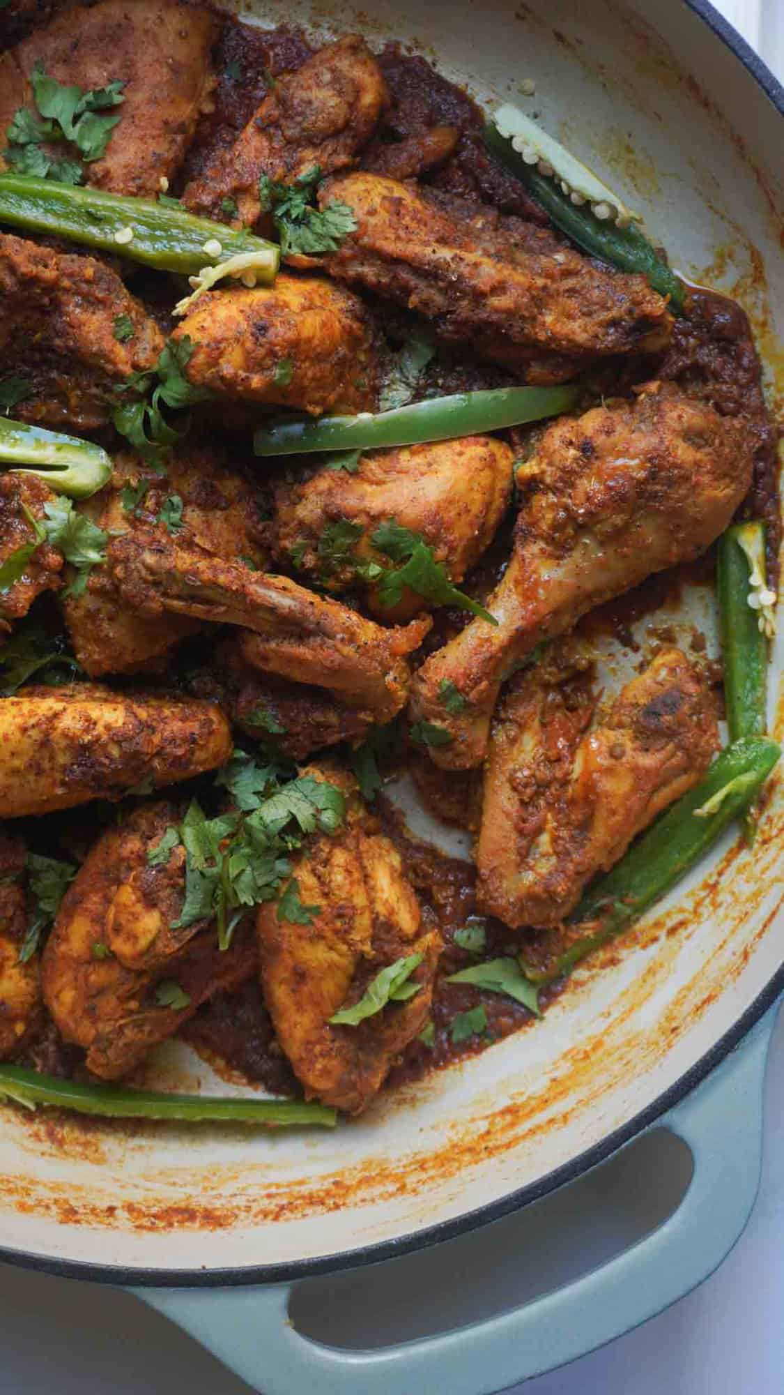 Karahi Chicken in a cast iron pan garnished with juliened green chilies and cilantro