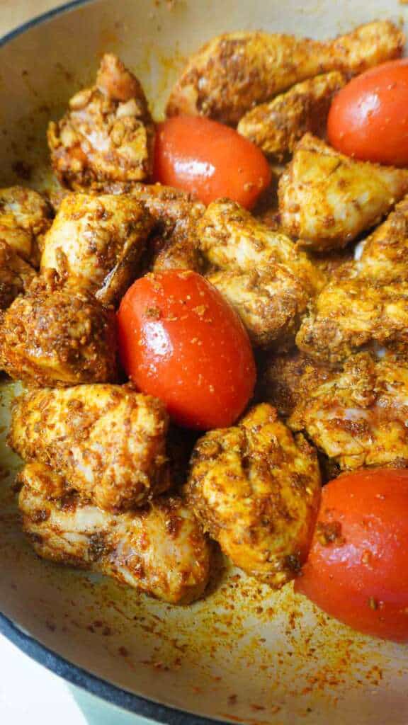 Chicken in karahi spices with whole tomatoes in a pan