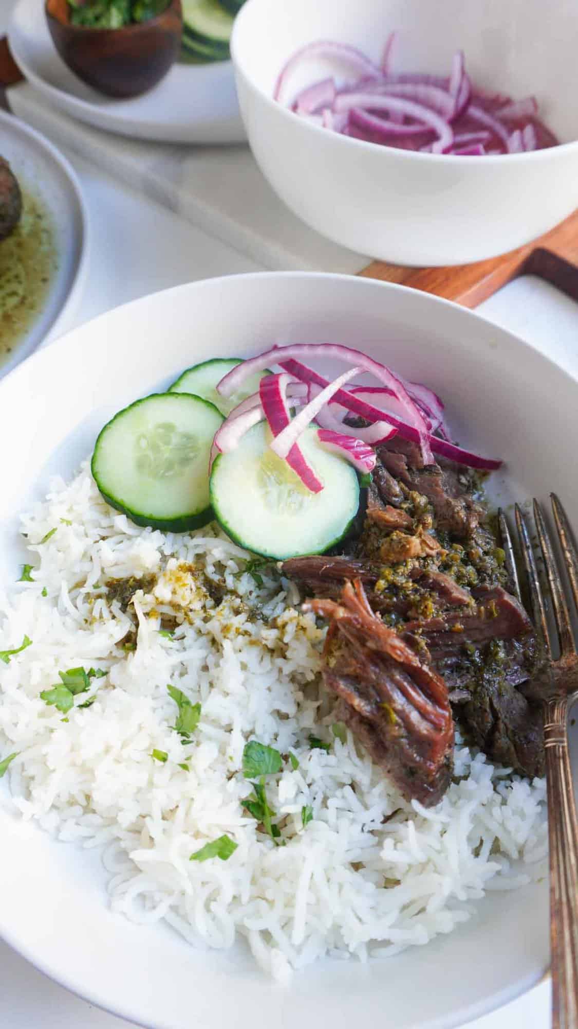 A serving of masala lamb bowl with shredded lamb, white rice, cucumber and red onion salad