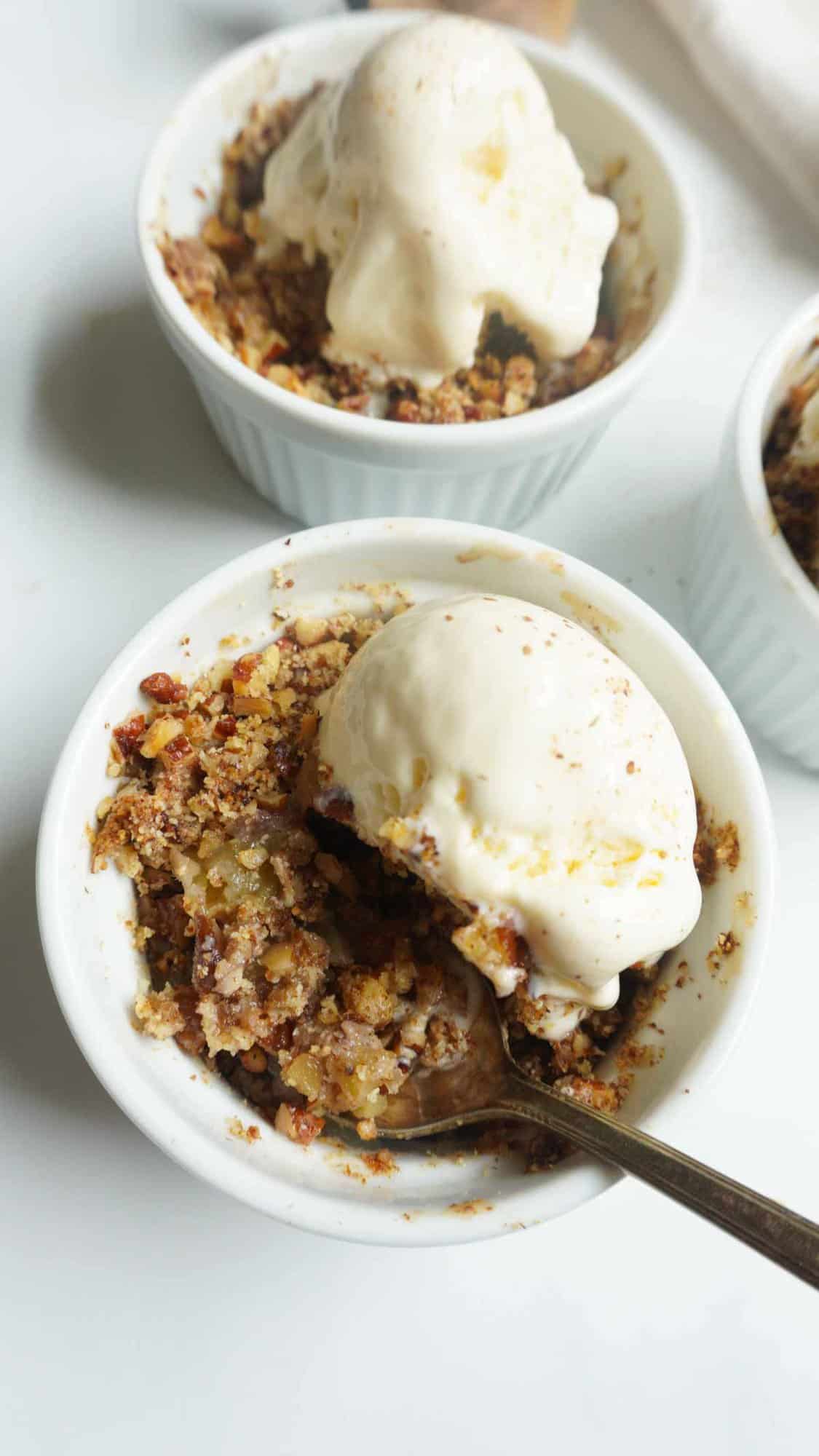 A close up of apple crisp bowl with a scoop of vanilla ice cream and 2 other bowls in the back ground