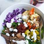 lamb bowl with bed of spinach and other vegetables topped woth garlic dressing and harissa