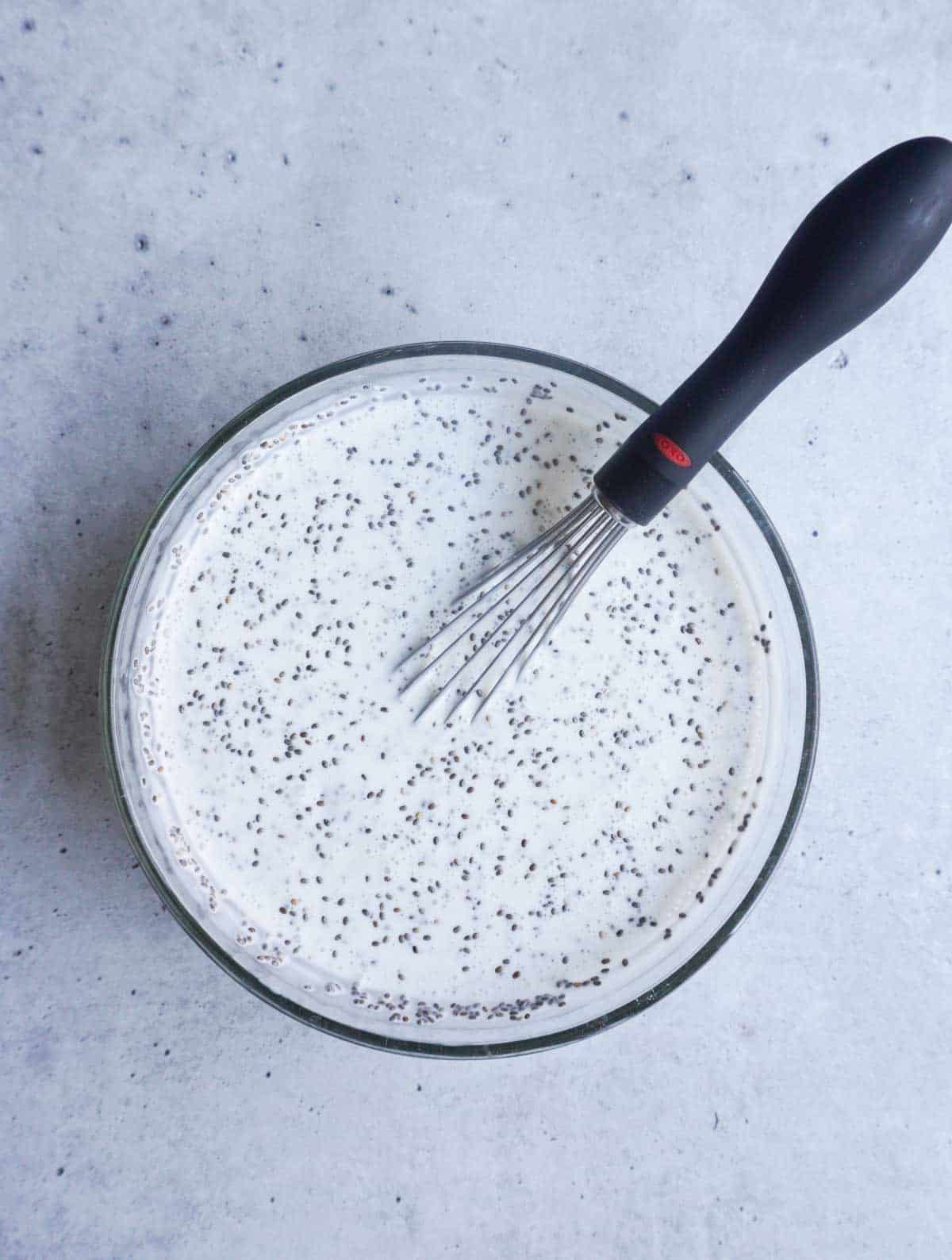 a bowl with coconut milk, chia seeds and a whisk 