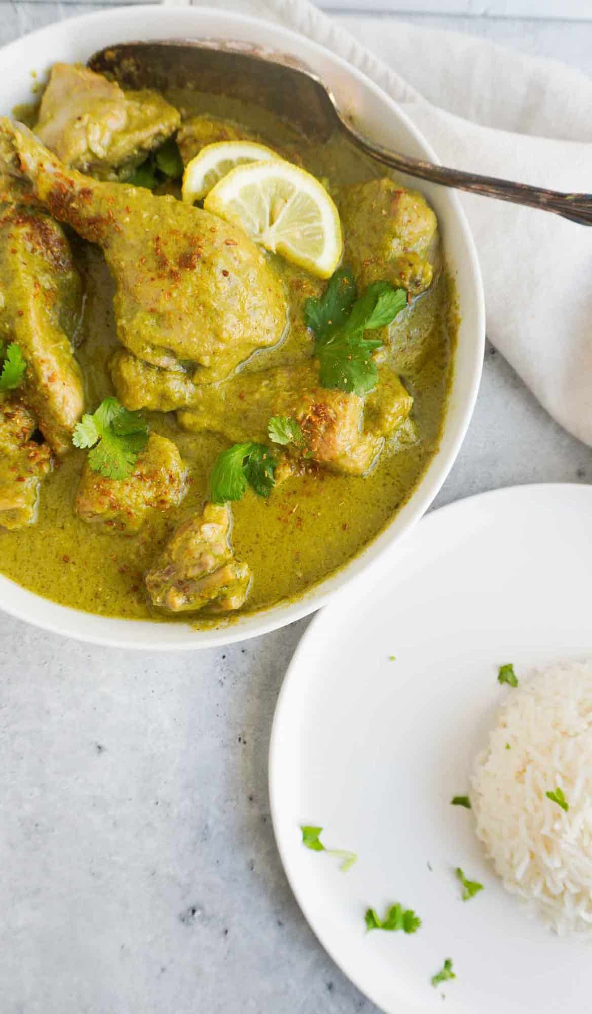 Hariyali chicken in serving bowl with cilantro, lemon and roasted cumin powder garnish with a mound of rice in a plate next to it