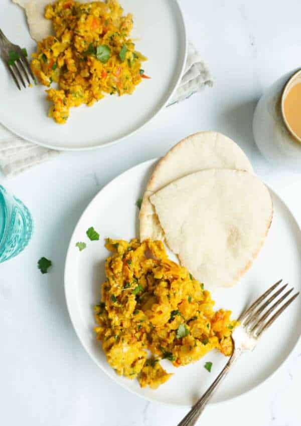 A personal serving of khageena with pita bread. A cup of chai and another plate of khagina in the background.