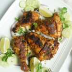 Platter with tandoori chicken thighs and drumsticks with lemon wedges, cucumber slices, onions and cilantro garnish