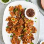 A platter with baked aloo pakoras and imli ki chutney and hari chutney in bowls.